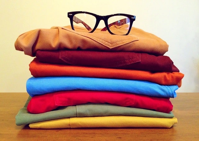 A vibrant stack of shirts in various colors alongside a pair of glasses placed neatly on a table.