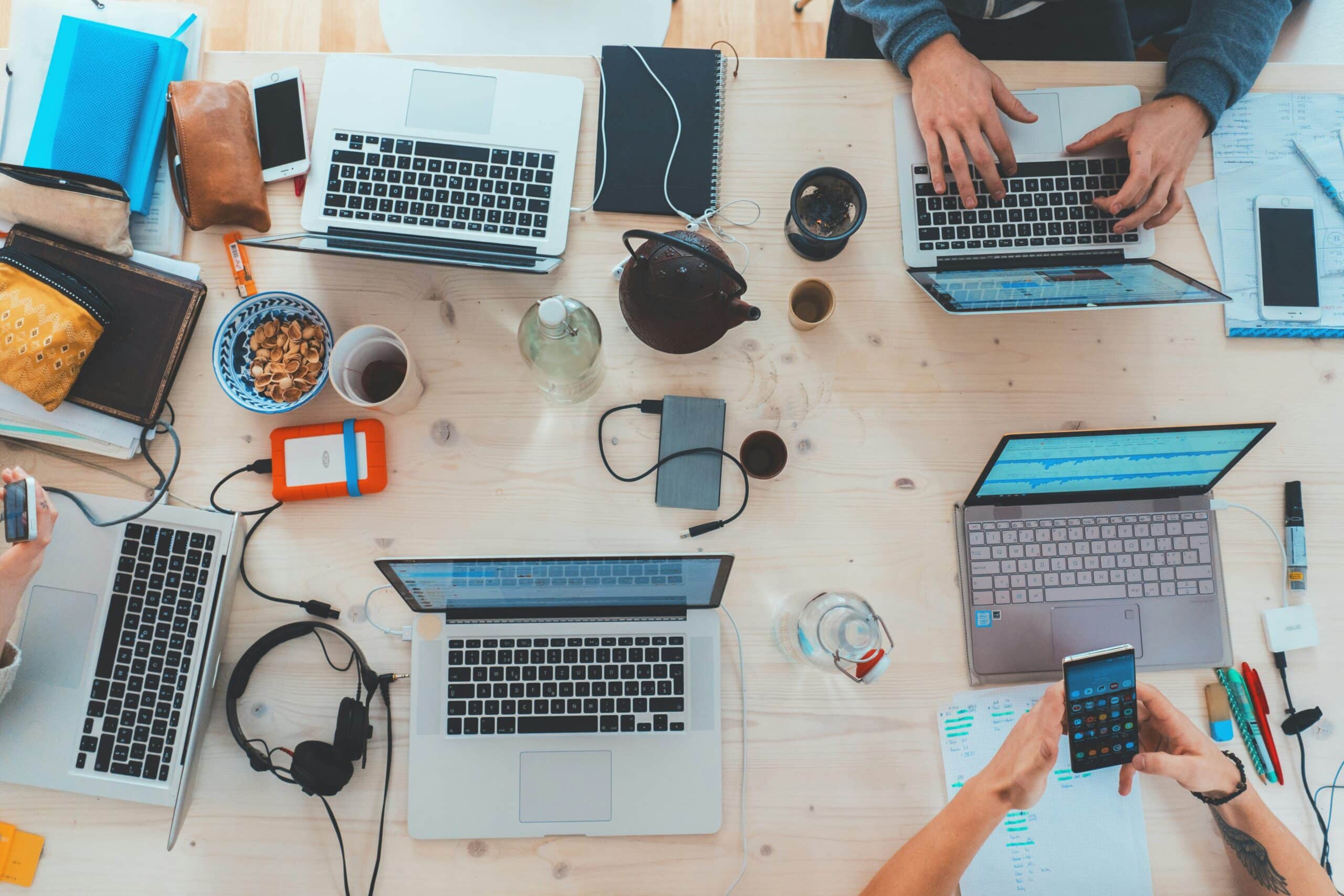 A diverse group of individuals collaborating on laptops at a table, surrounded by various tech gadgets and devices.