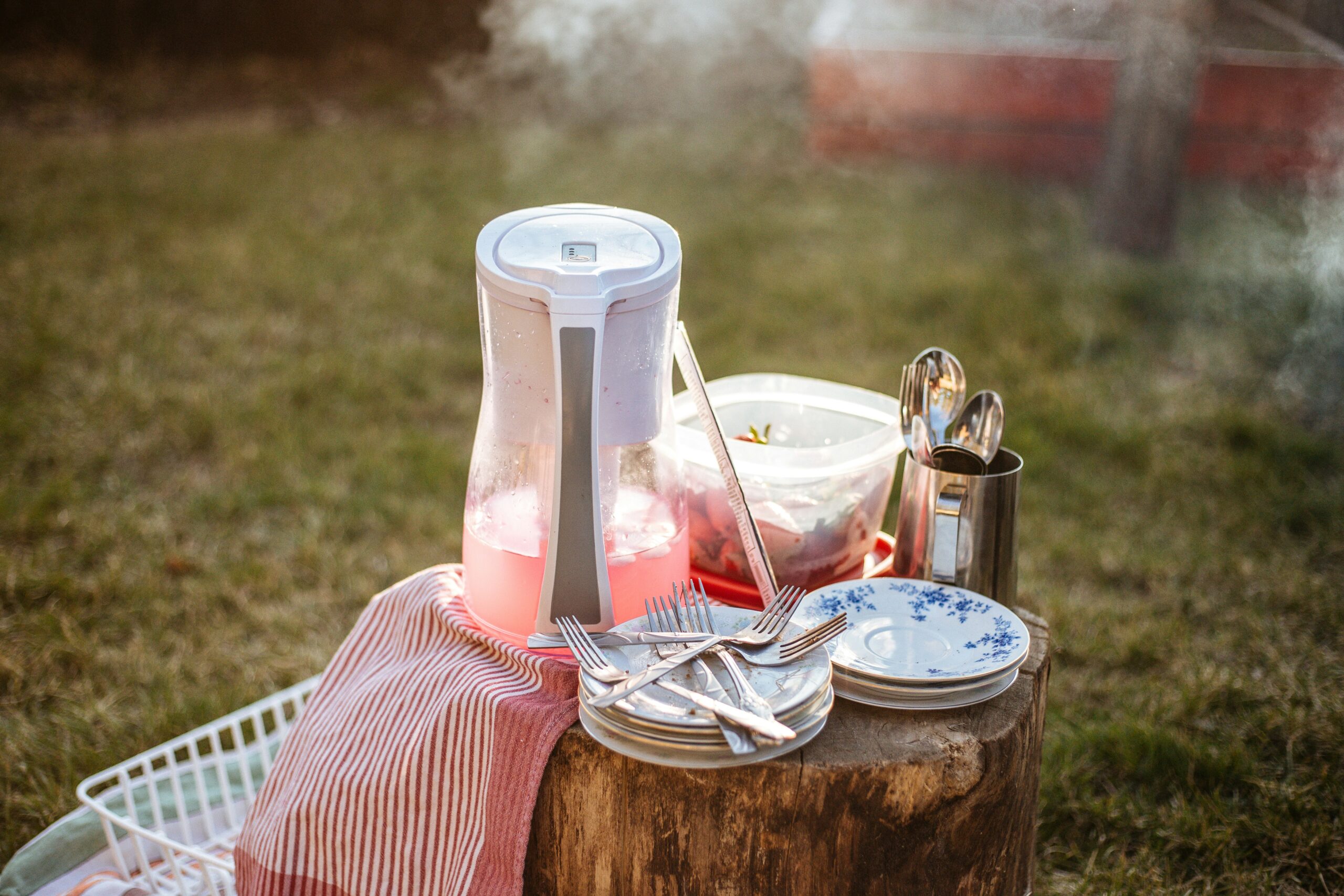 A picnic table featuring a pitcher of water and plates, surrounded by snacks, perfect for hydration during a delightful outdoor meal.